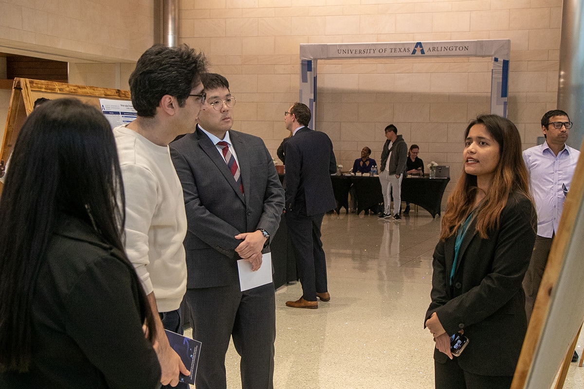People gathered in a hallway at the University of Texas at Arlington, interacting and viewing displays - opens in a new tab